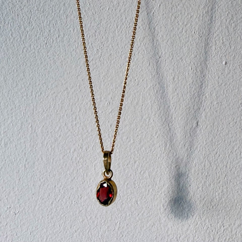 gold garnet pendant hanging against a wall in daylight